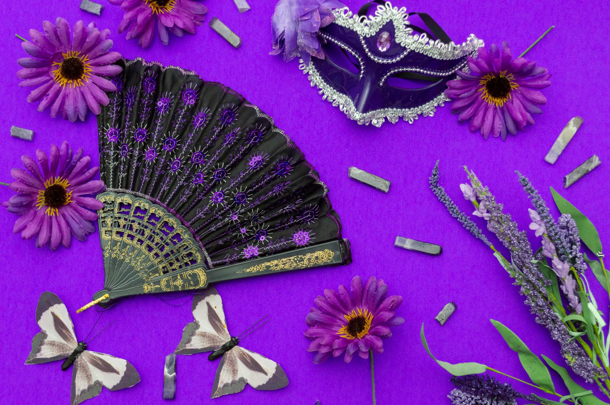hand fan, mask, and various flora arranged on purple background